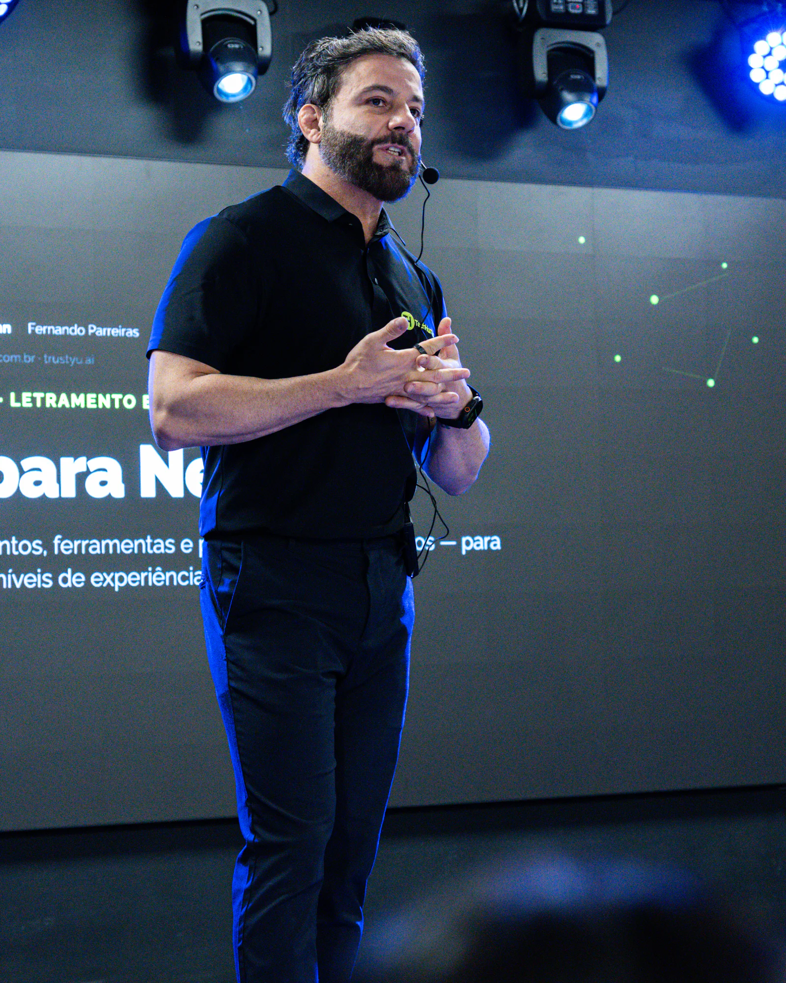 Fernando Parreiras apresentando no palco diante de uma tela iluminada.